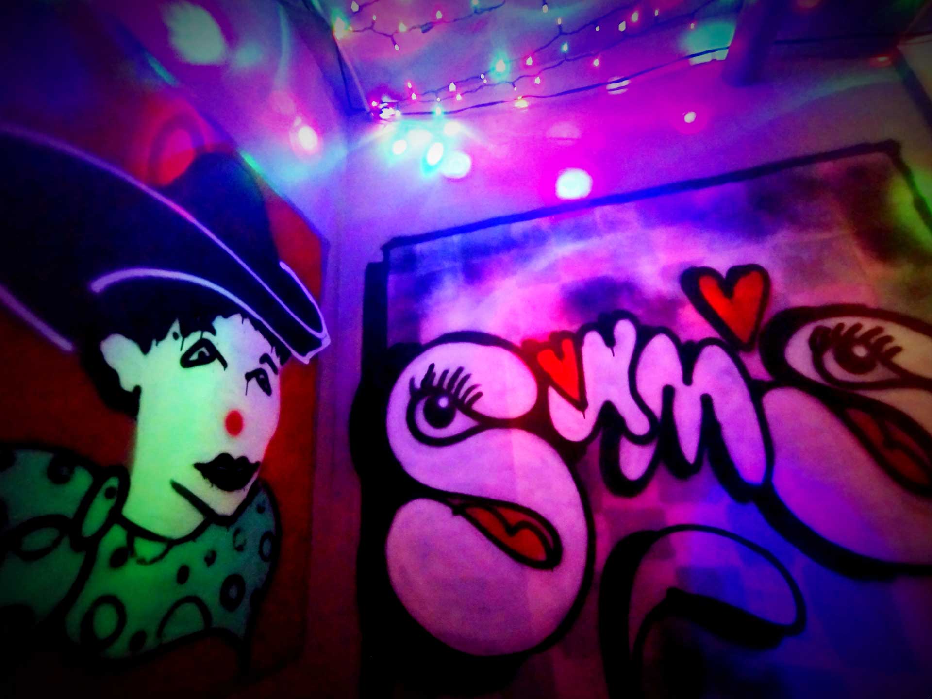 a photo of a spray painted wall in Sam's bar with a cowgirl clown and bubble letters and hearts that spell 'Sams's'